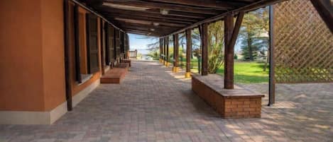 A covered walkway with brick flooring, wooden beams, and benches.
