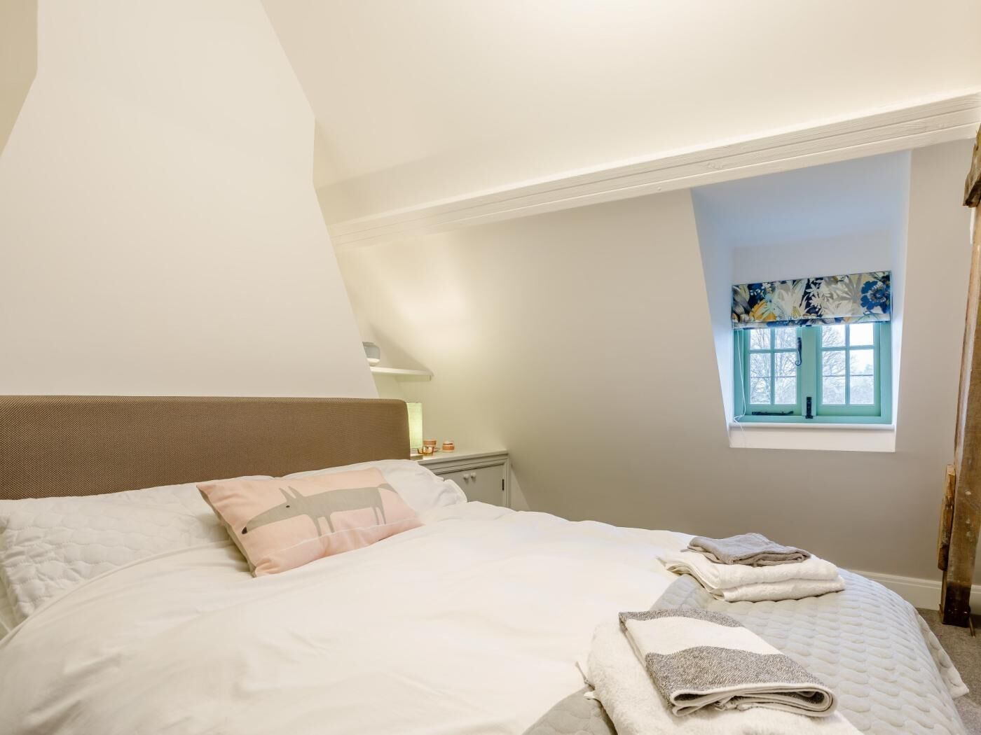 A bedroom with a bed, pillows, a window, and a nightstand.