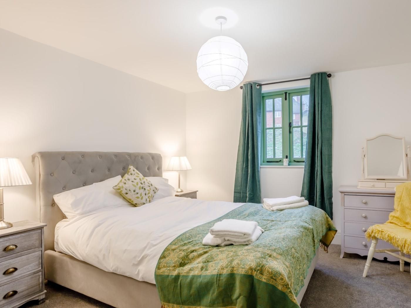 A bedroom with a bed, bedside tables, a mirror, and a window with curtains.