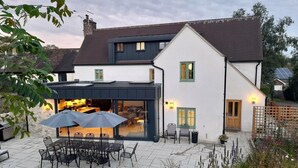 Ein zweistöckiges Haus mit einer Terrasse, die Gartenmöbel und eine überdachte Sitzgelegenheit bietet.