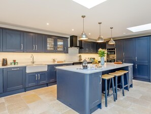Una cucina moderna con mobili blu scuro, un'isola centrale con sgabelli, illuminazione a sospensione e un lucernario.