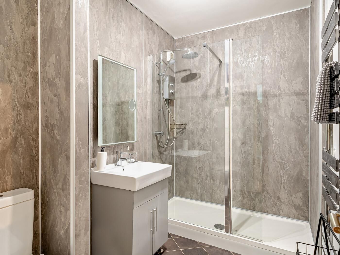 Un baño moderno con ducha envuelta en vidrio, un lavabo blanco y una pared de mármol.