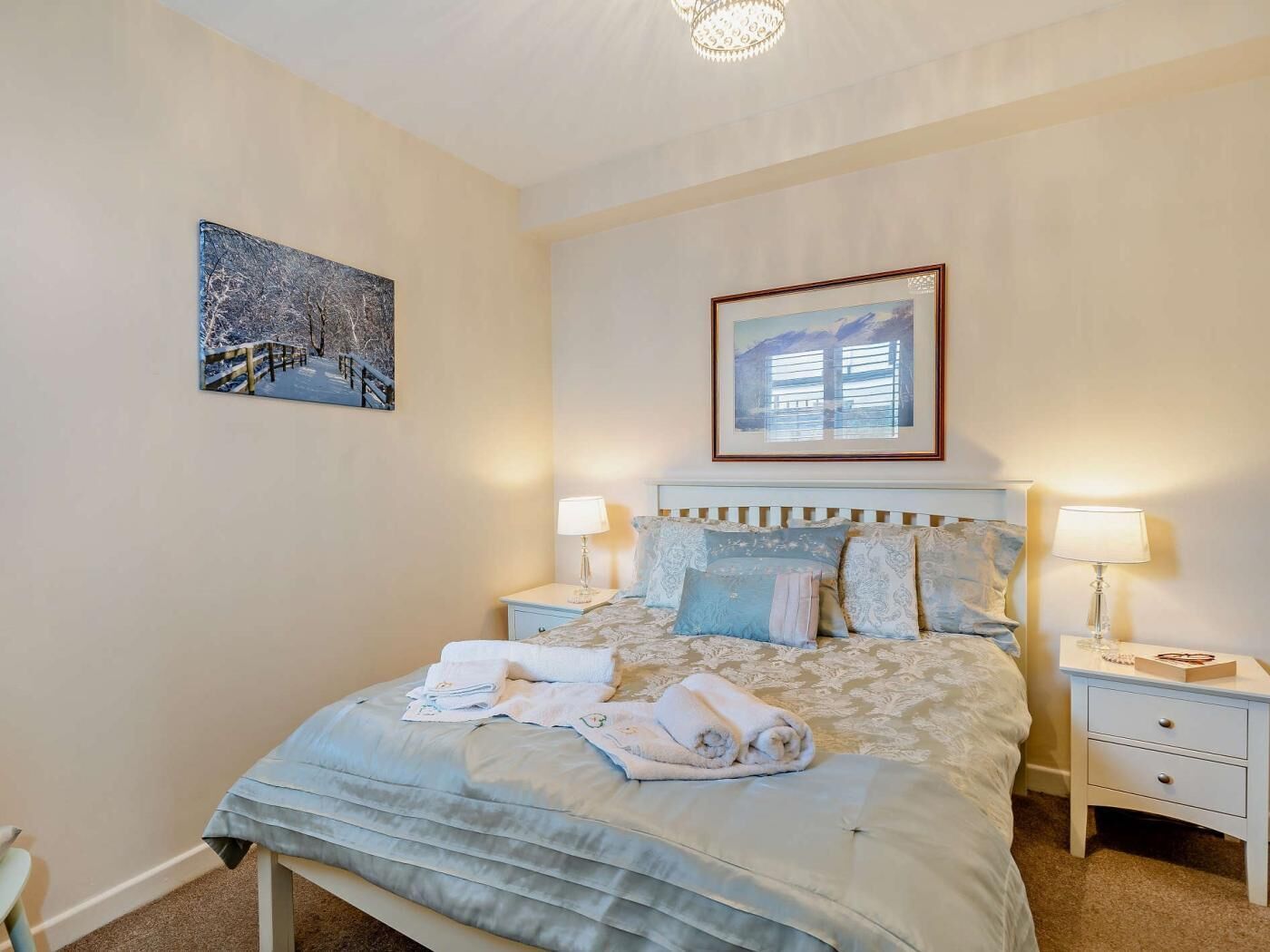 A bedroom with a bed, two bedside tables, a nightstand, a framed picture, and a ceiling light fixture.