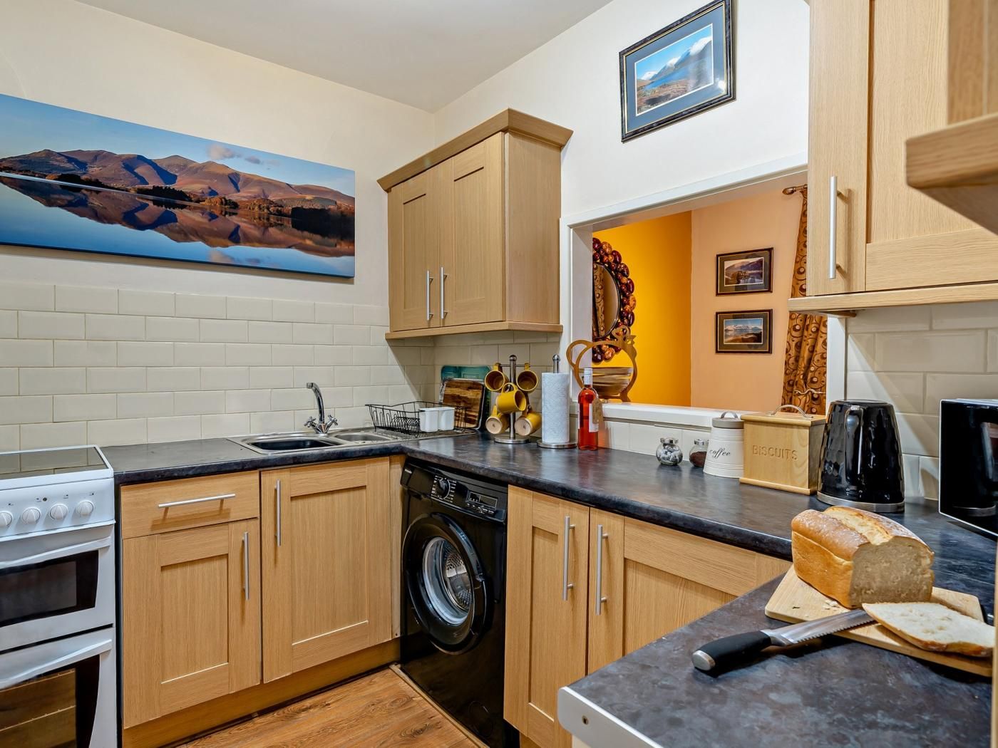 A kitchen with wooden cabinets, a washing machine, a coffee maker, and a loaf of bread on the counter.