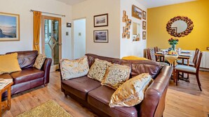 A living room with a brown leather sofa, a dining table with chairs, and a yellow accent wall with framed pictures. - 2 Bed in Keswick (oc-80515) (Keswick)