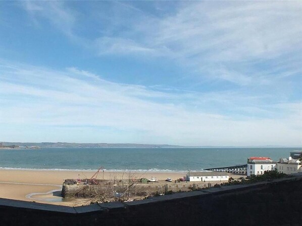 Vista costeira com uma praia, um cais e edifícios ao longe.