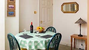A dining area with a checkered tablecloth, chairs, a wine bottle, a fruit bowl, and a mirror on the wall. - 1 Bed in Tenby (oc-fb024) (Tenby)