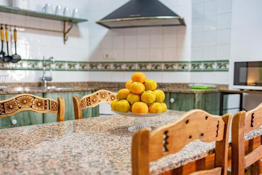Una cocina con encimera de granito, un frutero con limones, sillas de madera y salpicadero de azulejos.