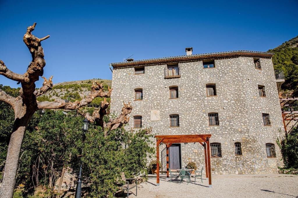 A stone building with multiple windows and a wooden pergola in the courtyard.