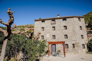 A stone building with multiple windows and a wooden pergola in the courtyard.