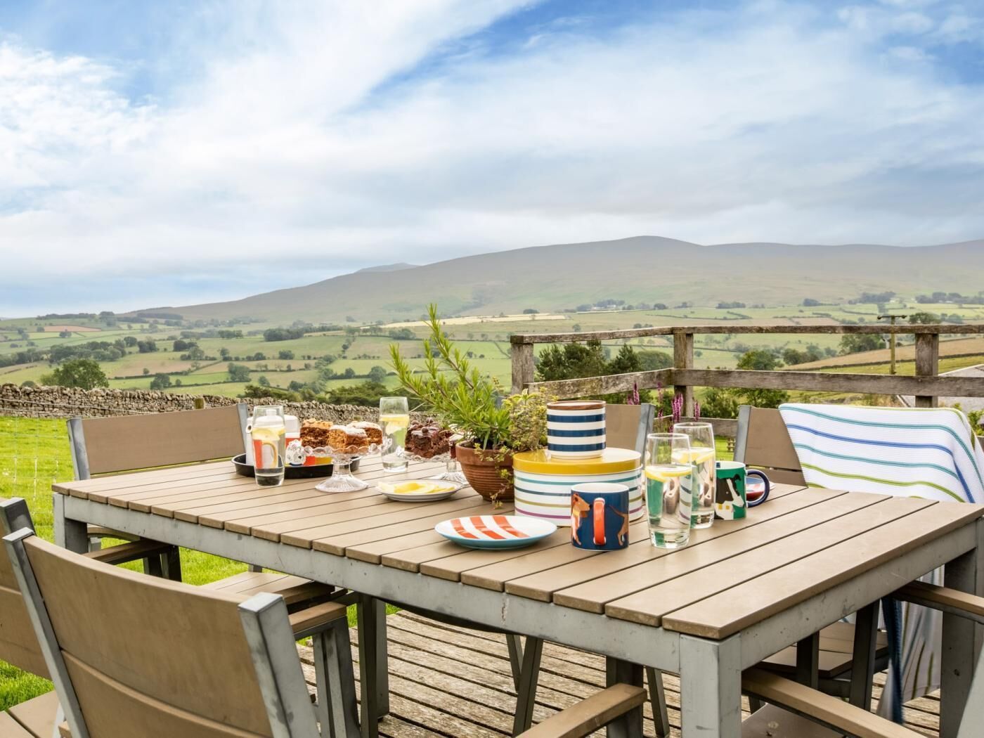 Une table en bois installée à l’extérieur, offrant une vue pittoresque sur des collines verdoyantes à l’arrière-plan.