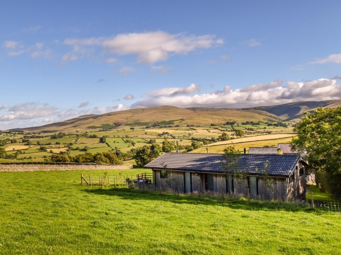 A rural landscape with a single building, surrounded by green fields and rolling hills.