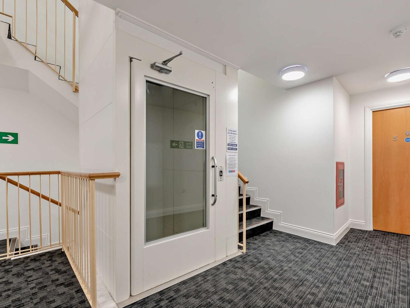 A hotel hallway with a glass door, a staircase, and a carpeted floor.