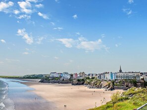 A coastal town with a sandy beach, buildings along the shore, and a prominent church spire. - 1 Bed in Tenby (oc-fb052) (Tenby)