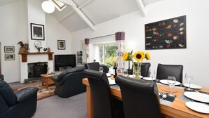 Una sala de estar moderna con chimenea, sofá de cuero negro, mesa de comedor con sillas y un ventanal con cortinas.
