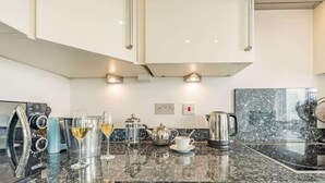 A modern kitchen with a granite countertop, stainless steel appliances, and a coffee maker. - 3 Bed in Tenby (oc-fb055) (Tenby)