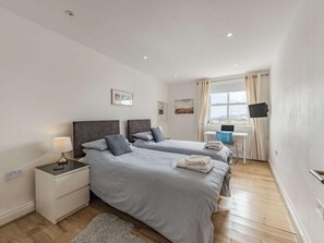 A bedroom with two beds, a desk, a TV, and a window with curtains. - 3 Bed in Tenby (oc-fb055) (Tenby)