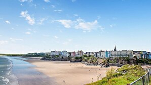 A coastal town with buildings along the beach, a clear sky, and a rocky shoreline. - 3 Bed in Tenby (oc-fb055) (Tenby)