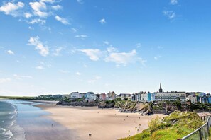 A coastal town with buildings along the beach, a clear sky, and a rocky shoreline. - 3 Bed in Tenby (oc-fb055) (Tenby)