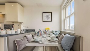 A modern kitchen with a built-in bench seating area, a dining table set for four, and a window providing natural light. - 3 Bed in Tenby (oc-fb055) (Tenby)