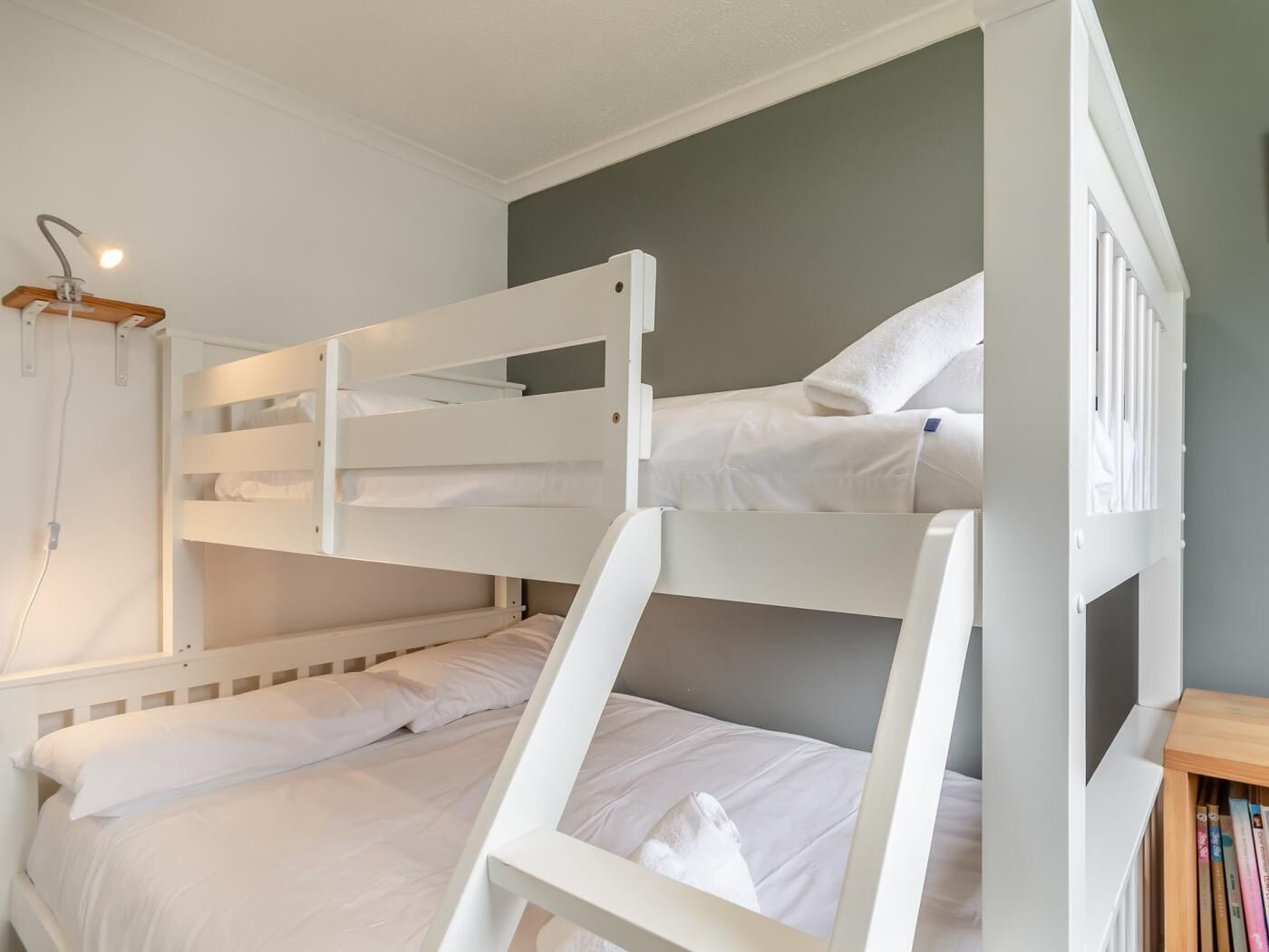 Une chambre avec un lit superposé, dotée de draps blancs et d’une tête de lit en bois.