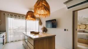 Uma cozinha moderna com uma ilha central, luminárias pendentes, uma TV de tela plana e vista para o exterior.