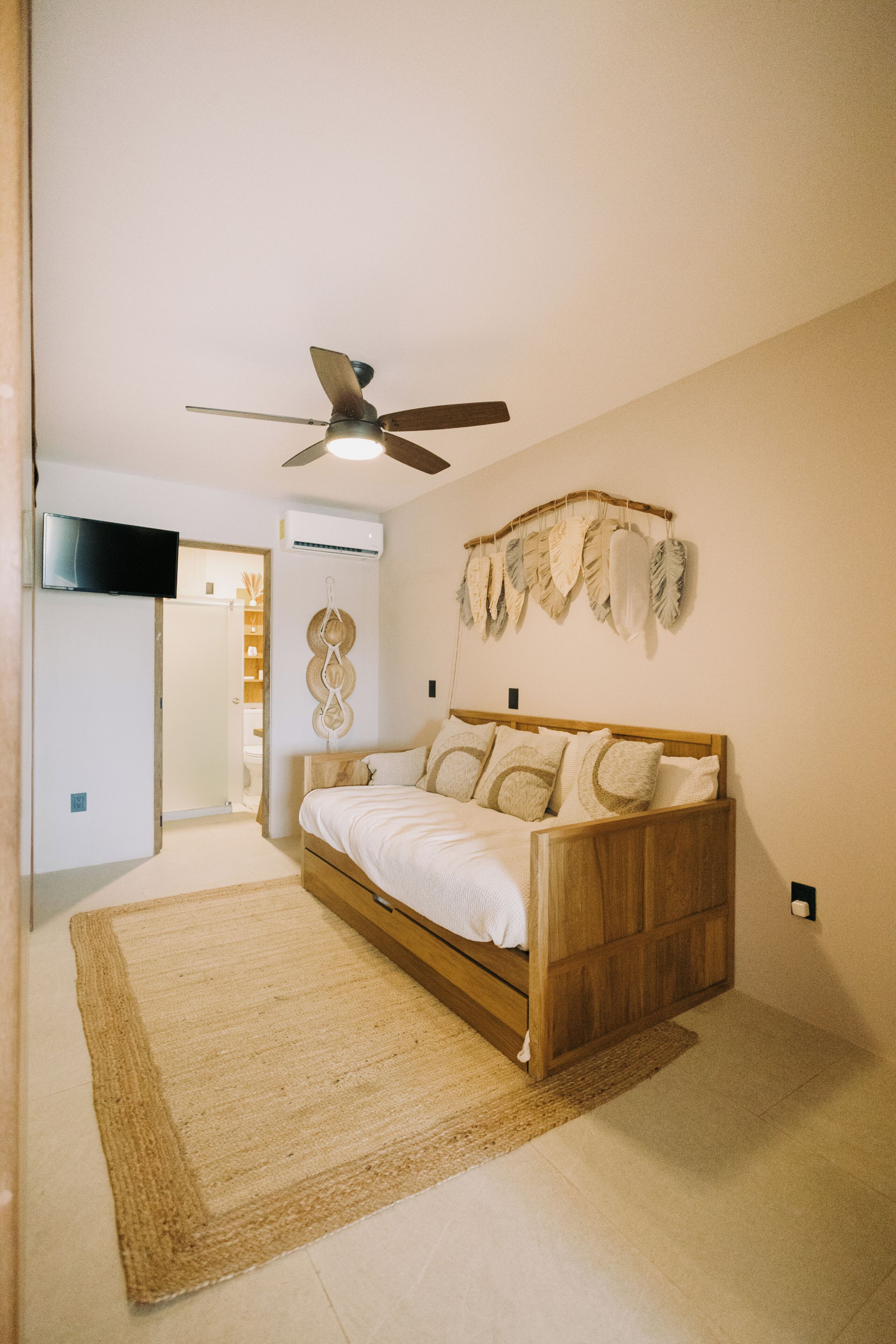 A bedroom with a bed, a ceiling fan, a wall-mounted TV, and a decorative wall hanging.
