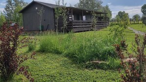 A rustic barn-style building with a porch, surrounded by lush green fields and trees. - The Lazy Wolf Cabin at Wolf Haven Cabins (Lovell)