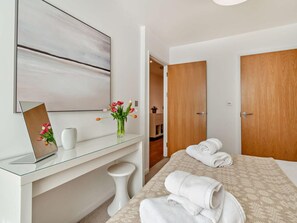 Ett hotellrum med ett skrivbord i glas, en säng med handdukar, en dörr i trä och en tavla på väggen.