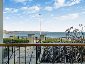 A balcony with a view of the sea, a metal railing, and some plants. - 2 Bed in Tenby (oc-fb108) (Tenby)