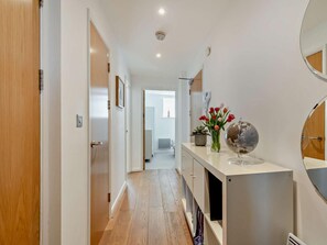 A hallway with wooden flooring, a white wall, and a small table with a globe and flowers. - 2 Bed in Tenby (oc-fb108) (Tenby)