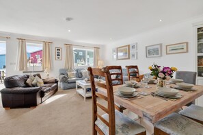 A spacious living area with a dining table set for four, a sofa, a coffee table, and a bookshelf. - 3 Bed in Freshwater East (oc-fb100) (Freshwater East)