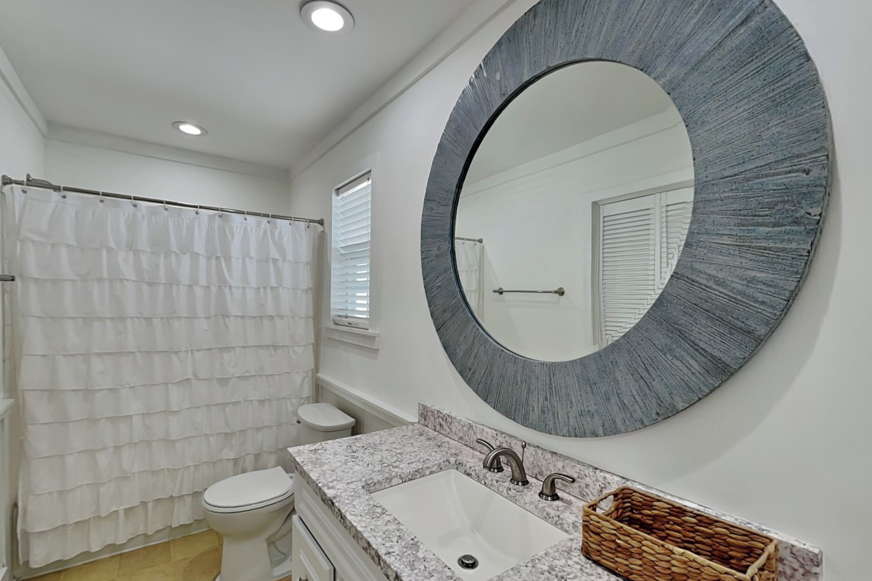 Une salle de bain avec des toilettes blanches, un rideau de douche, un lavabo doté d’un plan de travail en marbre et un grand miroir.