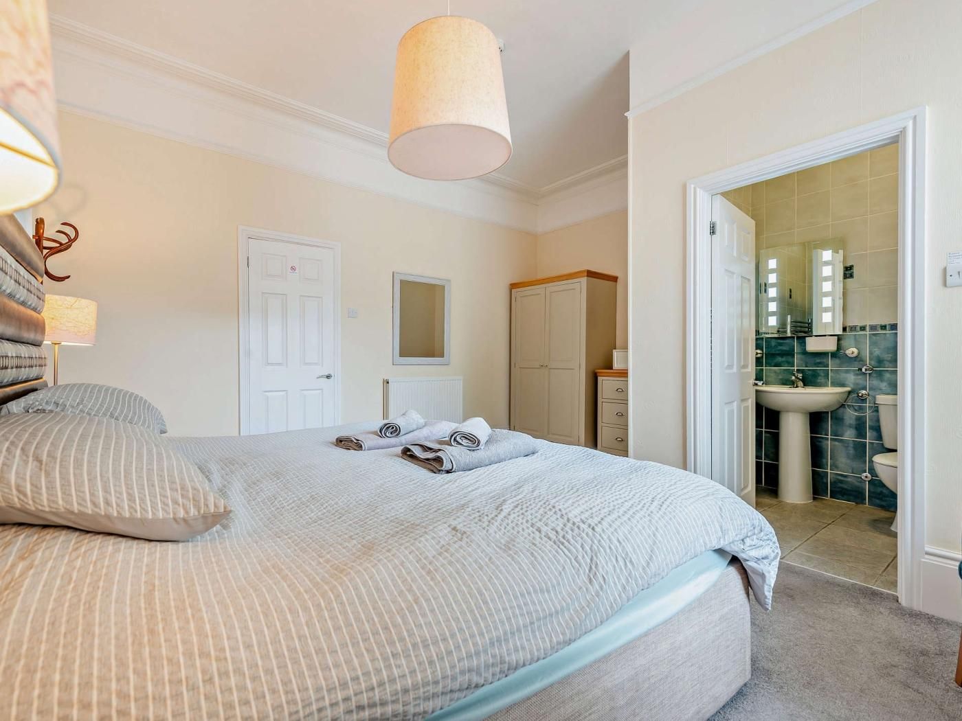A bedroom with a bed, bedside lamps, a wardrobe, and a bathroom visible through an open door.
