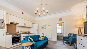 A compact living space with a kitchenette, a blue sofa, a wooden stool, and a television. - 1 Bed in Tenby (oc-fb154) (Tenby)
