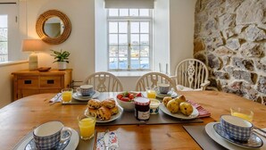 Un coin repas avec un mur en pierre, une table ronde dressée pour le petit-déjeuner et une vue par la fenêtre.