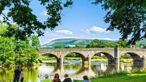 A stone bridge over a river with a grassy area and trees in the foreground. - 1 Bed in Llangammarch Wells (oc-bn089) (Treflys)