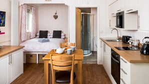 A compact room with a bed, a small table with a kettle, a chair, a shower, and a kitchenette. - 1 Bed in Llangammarch Wells (oc-bn089) (Treflys)