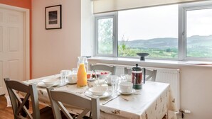Un comedor con una mesa lista para el desayuno, vistas al campo a través de grandes ventanales y un radiador debajo de las ventanas.