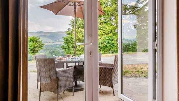 Puerta corrediza de vidrio abierta que da a un patio exterior con mobiliario de mimbre y una mesa dispuesta para comer.