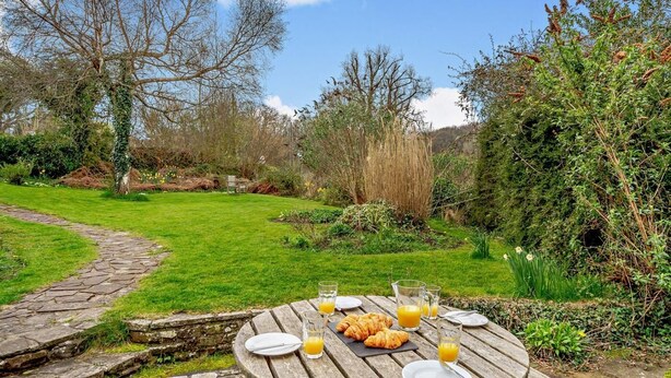 Ein Holzpicknicktisch mit Tellern, Gläsern und Croissants im Freien.