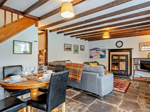 A cozy living room with a fireplace, a dining area with a wooden table and chairs, and a grey sofa. - 2 Bed in Crickhowell (oc-bn052) (Llangynidr)