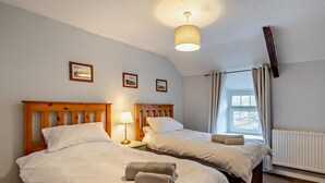 Ein Hotelzimmer mit zwei Betten, einer Deckenleuchte, einem Fenster mit Vorhängen und gerahmten Bildern an der Wand.