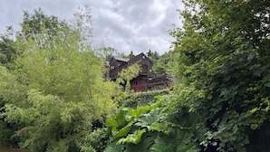 A river with dense foliage on one side and a wooden house with a deck in the background. - 2 Bed in Brecon (oc-bn102) (Talybont-on-Usk)