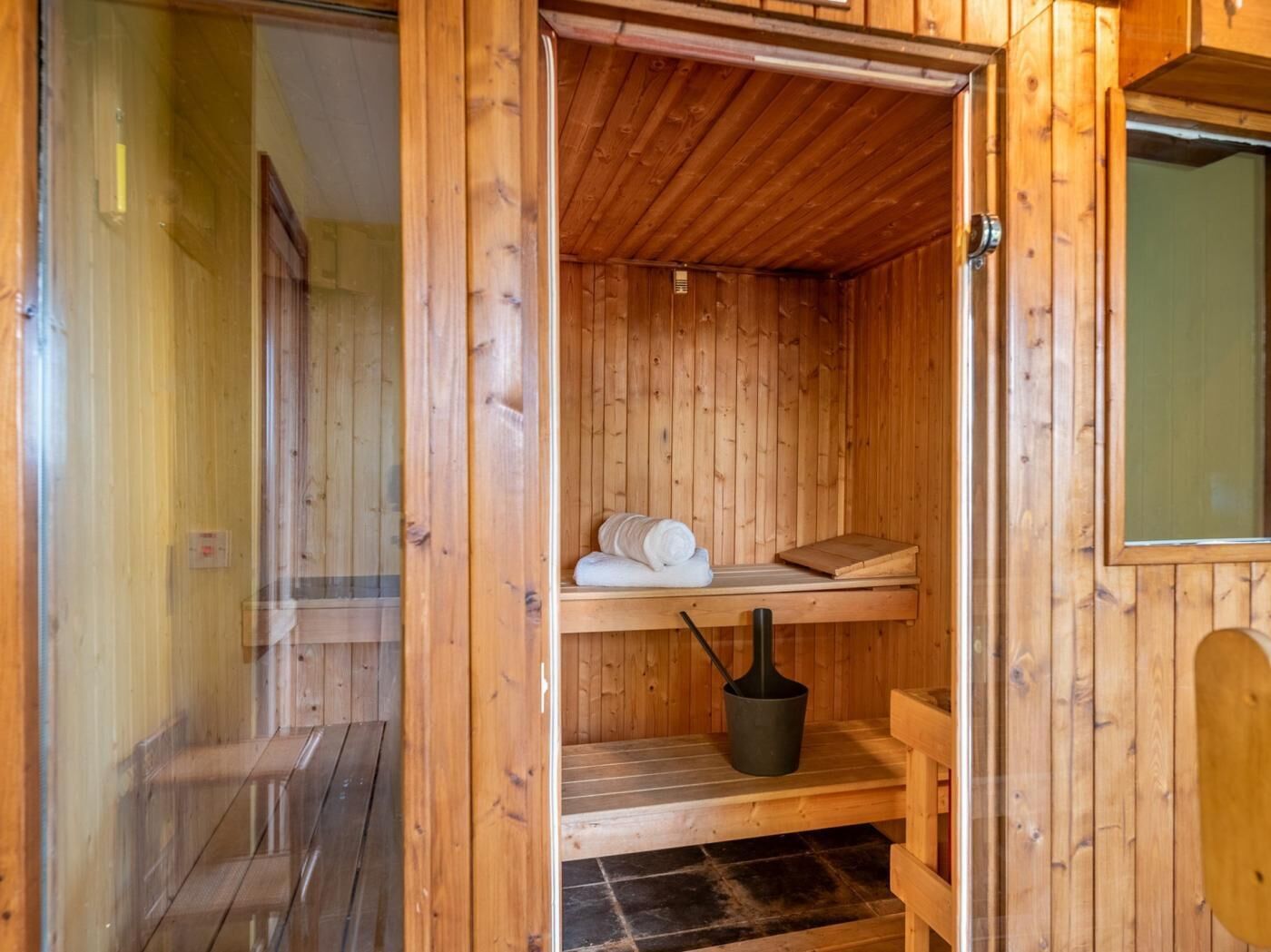 Un sauna de madera con un banco, un balde y toallas.