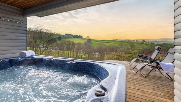 Un bain à remous doté d’une terrasse en bois, offrant une vue sur un paysage verdoyant, avec des arbres et des collines.