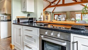 Eine Küche mit weißen Schränken, einer Granit Arbeitsplatte, einem eingebauten Backofen und einer Holzbalkendecke.