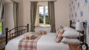 Un dormitorio con cama, ventana con cortinas, mesita de noche con lámpara y un reloj.