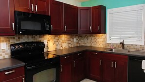 Una cocina con armarios rojo oscuro, un microondas negro y una estufa.