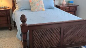Una cama de madera con cabecera, una mesita de noche con lámpara, y una pequeña mesa con lámpara y un objeto decorativo.